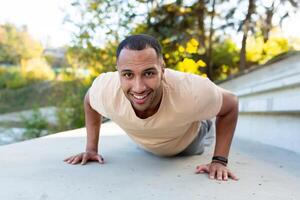 Young african american male athlete doing exercises in stadium on concrete stairs. Pushes up, looks smilingly at the camera. photo