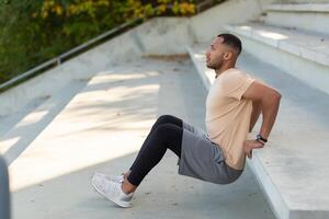 Young african american male athlete doing exercises in stadium on concrete stairs. Squats, shakes hands. photo