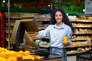 Portrait of satisfied female shopper in supermarket, Hispanic woman weighing fruit in store, smiling and looking at camera using self-service scales. photo