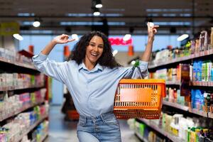 Portrait of a happy and smiling woman shopper in a supermarket, herpanic woman shopping and looking at the camera happily chooses products inside the store among the shelves with a shopping basket. photo