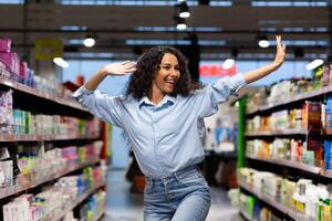 Happy young woman dancing with open arms in a supermarket aisle, expressing joy and freedom amidst the shelves. photo