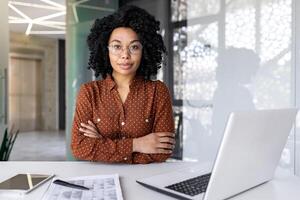 Portrait of mature successful businesswoman financier accountant employee serious and focused looking at camera sitting at desk with arms crossed. photo