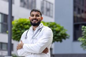 Portrait of a smiling young Muslim male veterinarian standing outside a hospital and looking confidently into the camera with his arms crossed over his chest. photo
