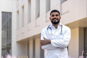 Portrait of a young doctor student, an intern standing outside the medical building and looking at the camera with his arms crossed on his chest. photo
