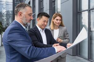 Diverse group of business people outside office building, discussing and talking man and woman discussing new construction plan, team of business people holding and looking at construction project photo