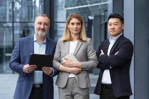 Diverse team man and woman outside office building business people with crossed arms looking thoughtfully at camera colleagues employees three persons photo