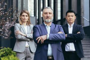 Portrait of serious diverse business team, employees with boss together looking at camera seriously and thoughtfully, group of business people outside office in business suits photo