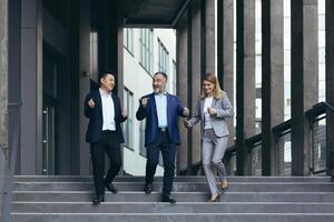 diverse business team, man and woman walking together outside office building, satisfied with victory celebrating, business people dancing on stairs and smiling happy photo