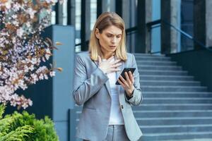 Frustrated and shocked business woman reading bad news online from phone, businesswoman outside office in business suit photo