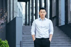 Portrait of serious asian businessman, man outside office looking at camera photo