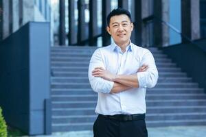Happy asian in shirt outside near office, portrait of successful businessman, looking at camera and smiling photo