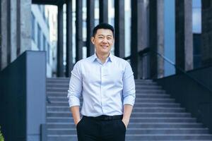 Happy asian in shirt outside near office, portrait of successful businessman, looking at camera and smiling photo