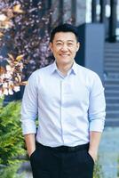 Vertical frame, Asian man in white shirt looks at camera and smiles, hands in pockets photo