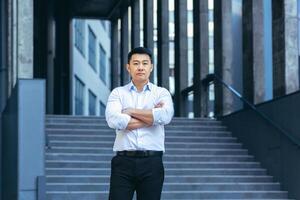 Portrait of serious asian businessman, man outside office looking at camera photo