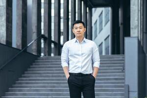 Portrait of serious asian businessman, man outside office looking at camera photo