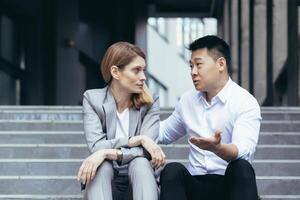 Two business colleagues Asian man and woman sitting on stairs talking and discussing in work break photo