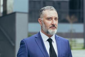 Close-up photo portrait of gray-haired successful businessman boss, man concentrating and thinking looking at camera, businessman owner in business suit outside office