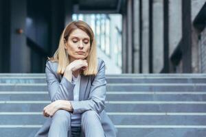 de cerca retrato de triste trastornado negocio mujer sentado cansado en escalera de oficina edificio foto