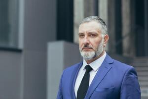 Close-up photo portrait of gray-haired successful businessman boss, man concentrating and thinking looking at camera, businessman owner in business suit outside office