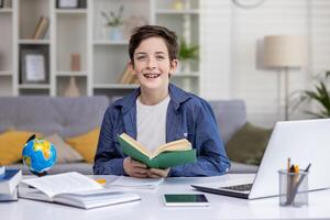 Portrait of a schoolboy at home in the living room, the boy is studying sitting at the desk, reading a book and doing homework, the teenager is smiling and looking at the camera. photo