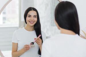 Close-up photo. Portrait of a young beautiful woman standing in front of a mirror and applying make-up with a brush on her face. Going to work, a meeting, a walk, smiling photo