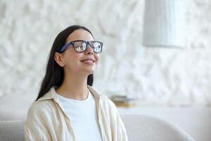 Time for yoga. Close-up photo. Portrait of an attractive young woman wearing glasses sitting on a sofa at home in the lotus position with closed eyes. Rests, relaxes photo