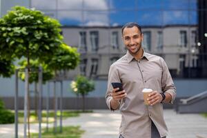 un persona es participación un teléfono inteligente y un café taza, en pie al aire libre con arboles y edificios en el antecedentes foto