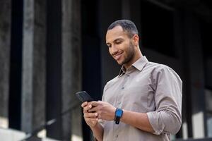 Smiling African American businessman using smartphone outside modern office building, young professional on the go. photo