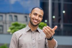 alegre africano americano joven hombre en casual negocio atuendo en pie con confianza fuera de un moderno oficina edificio. foto