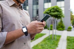 Close up of man's hands, businessman in shirt holding phone, using app on smartphone, walking in city outside office building. photo