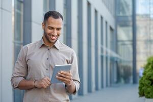 Smiling young man using tablet in urban setting, portraying connectivity, technology, and casual business outdoors. photo