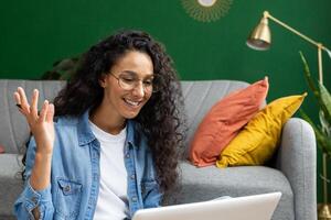 de cerca de alegre mujer estudiando a hogar, acecho tutorial curso, sonriente contentamente sentado en sofá en vivo habitación, hablando con profesor mentor utilizando llamada en ordenador portátil. foto