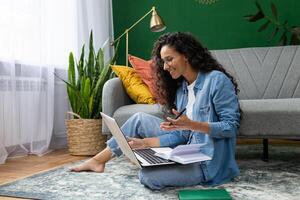 Young beautiful woman sitting on the floor at home in the living room, student studying remotely, using laptop to watch webinar and course, online call consultation with teacher. photo