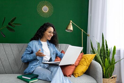 sonriente mujer en lentes teniendo un llamada en ordenador portátil a hogar, expresando alegría y comodidad en un acogedor vivo habitación ajuste. foto