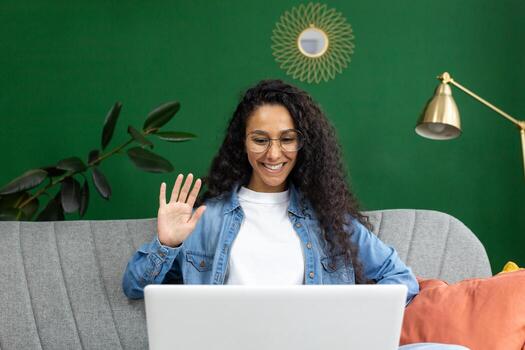 alegre mujer en lentes ondulación durante un llamada en ordenador portátil a hogar, expresando alegría y amabilidad en un casual ajuste. foto