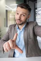 A professional middle-aged man participates in a call, gesturing while conversing. He is in a stylish, contemporary office setting, wearing a suit and a friendly expression. photo