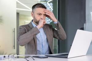 Worried businessman looking confused while working on a laptop in a contemporary office setting, displaying signs of stress or problem-solving. photo