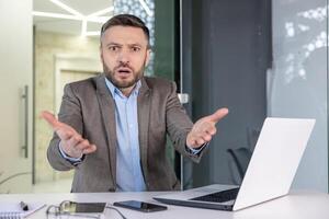 Portrait of a befuddled businessman in an office setting looking directly at the camera with a confused expression and hands up in a questioning manner. photo