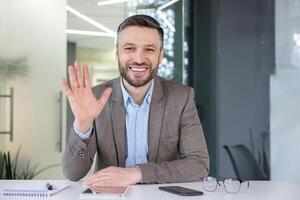 Cheerful, professional man in business attire waving hello. A modern workplace ambiance with a touch of warmth and friendliness. photo
