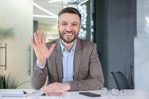 Cheerful, professional man in business attire waving hello. A modern workplace ambiance with a touch of warmth and friendliness. photo