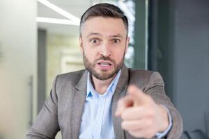 An irate businessman pointing a finger while talking angrily on a call, showing frustration and aggression. photo