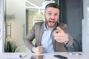 An upset businessman is expressing anger and frustration while looking into the camera, possibly during a call. photo