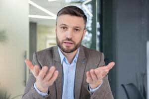 A professionally dressed man engaging in a call in a well-lit, modern office setting, conveying openness and discussion. photo