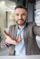 Confident businessman extending hand, engaging in an online call in a contemporary office setting. Ideal for business, communication, and corporate themes. photo