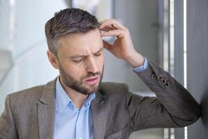 Confused businessman scratching head, expressing doubt and problem solving in a modern office setting, portraying perplexity. photo