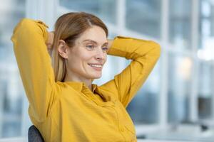 Relaxed businesswoman smiling during a break at work. Confident, happy, and content in a modern office environment wearing a bright yellow shirt. photo