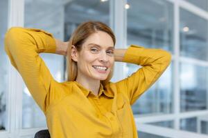 Relaxed businesswoman smiling confidently while stretching in an office environment. Displaying positive energy and professional comfort in a modern workspace. photo