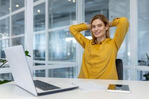 Happy woman in yellow shirt taking a break while working at modern office. Relaxed and cheerful atmosphere. photo