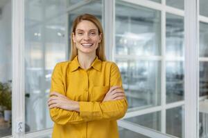 Smiling businesswoman standing with arms crossed in a modern office. She exudes confidence and professionalism, ready for any challenge at work. photo