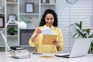 Successful and happy hispanic businesswoman working remotely at home, woman received good news notification mail reading and happy, working sitting at table with laptop. photo